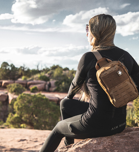 Affiliate blogger writing a survival gear review on a laptop surrounded by tactical equipment, backpack, and outdoor tools—symbolizing content monetization through preparedness gear promotions.