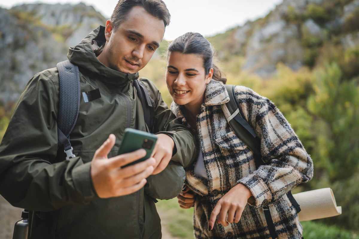 Couple hiking in forest using mobile phone for navigation, highlighting outdoor adventure and survival skills.