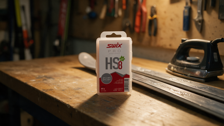 Swix HS8 fluoro-free glide wax on a ski tuning workbench beside skis and a waxing iron